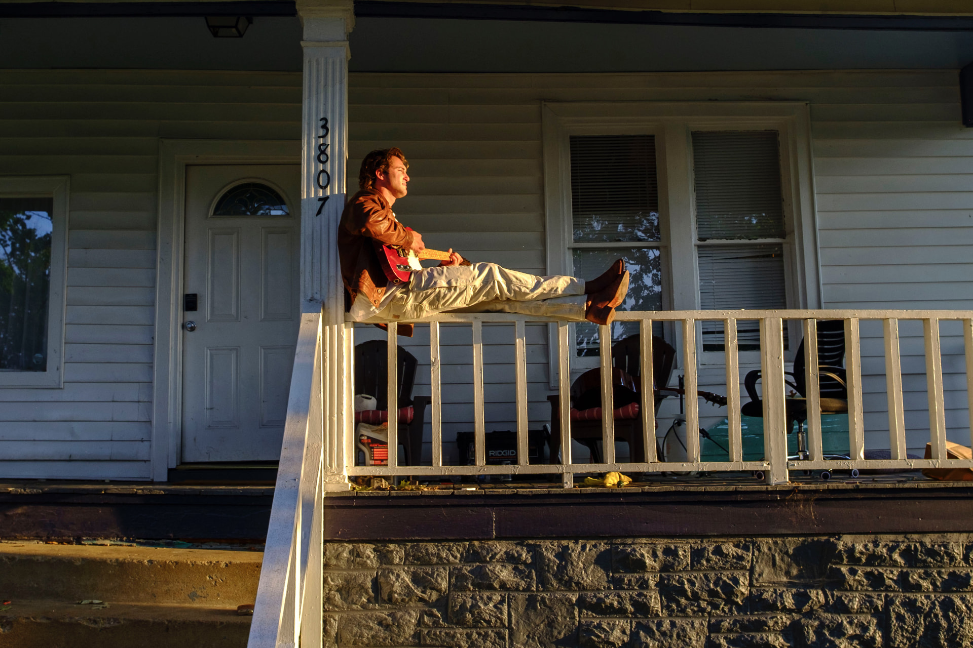 Dante DeRosa sitting on a porch railing at golden hour playing his red Telecaster