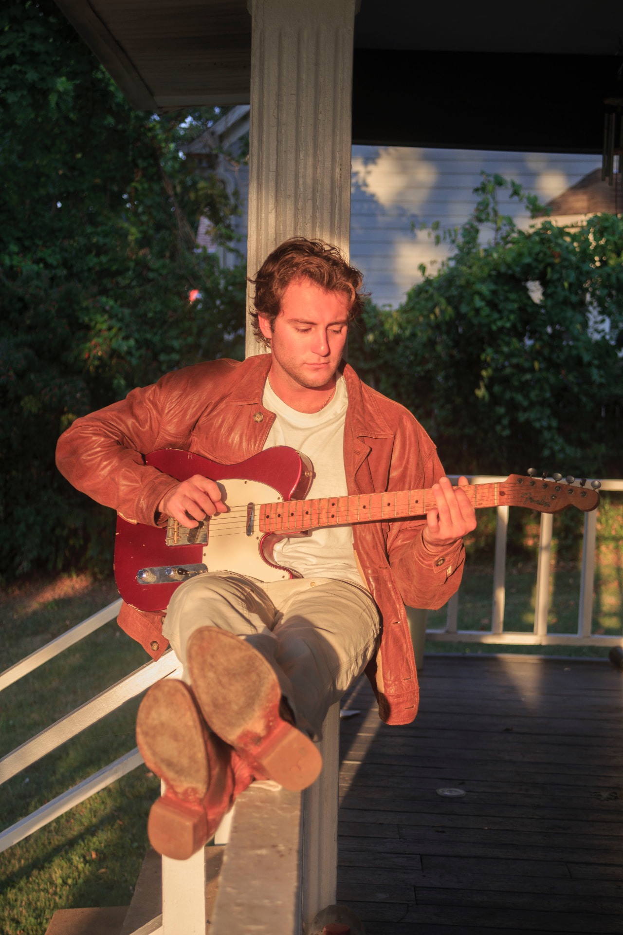 Dante DeRosa playing his red electric guitar on a porch railing in the evening sun